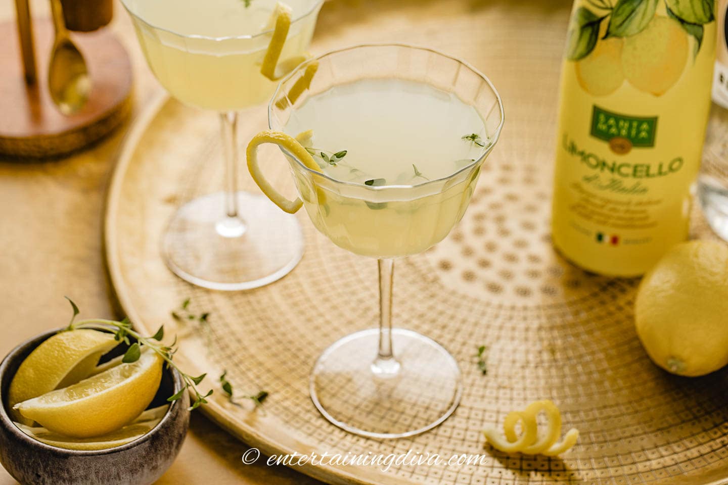 Two limoncello martinis on a tray with a bottle of lemons and a bottle of limoncello.