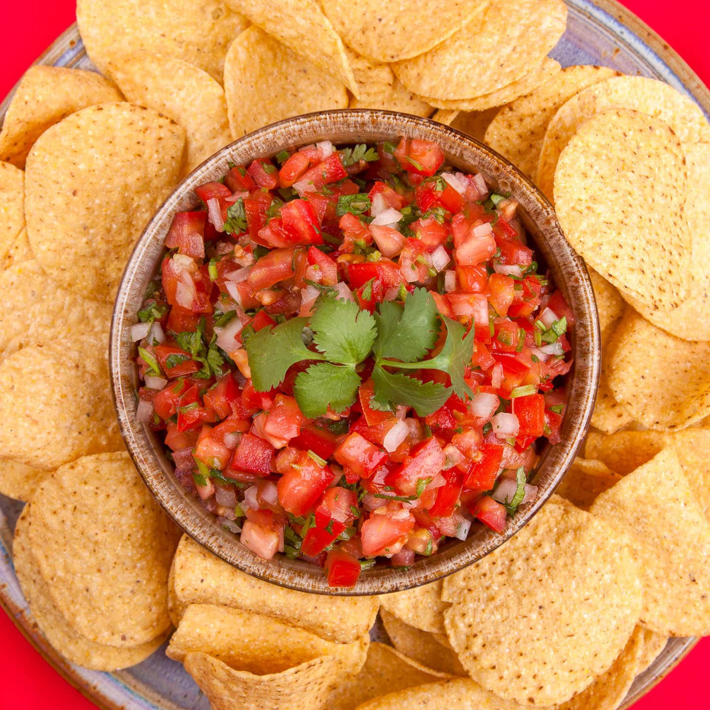 overhead picture of pico de gallo in a bowl surrounded by chips on a plate