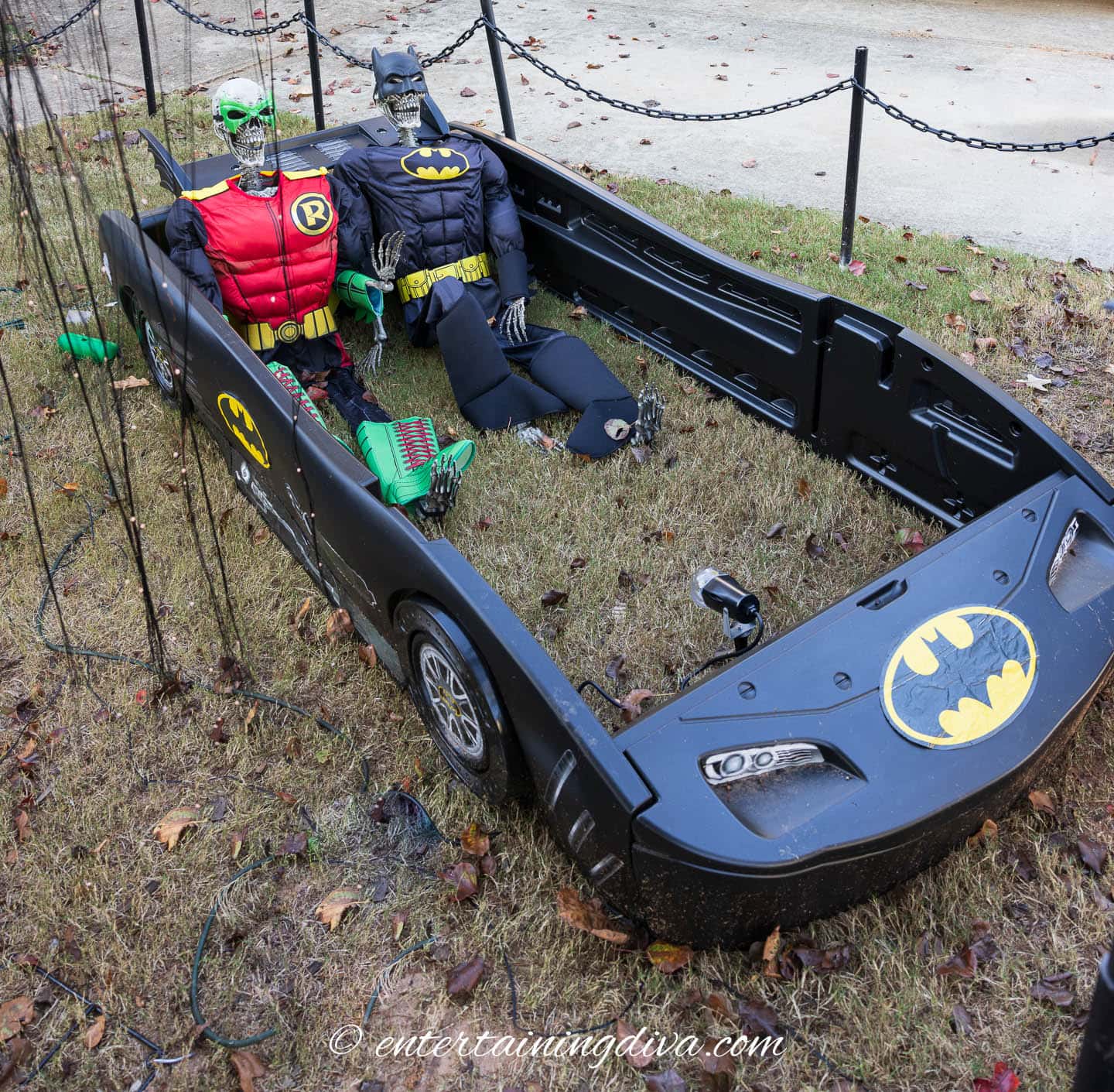 Skeletons dressed as Batman and Robin inside a batmobile toddler's bed in the front yard