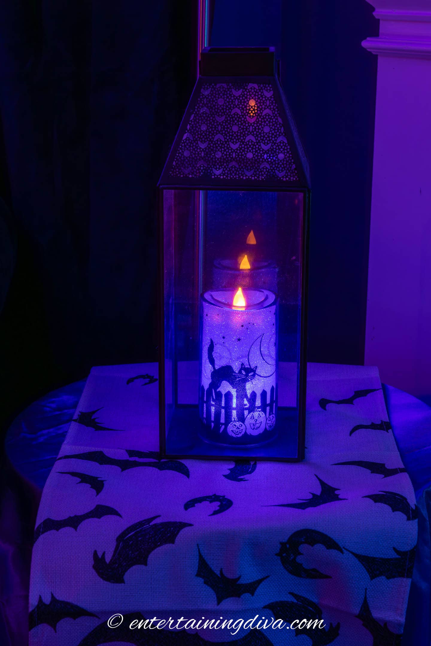 a flameless pillar candle in a lantern on a table with a bat runner