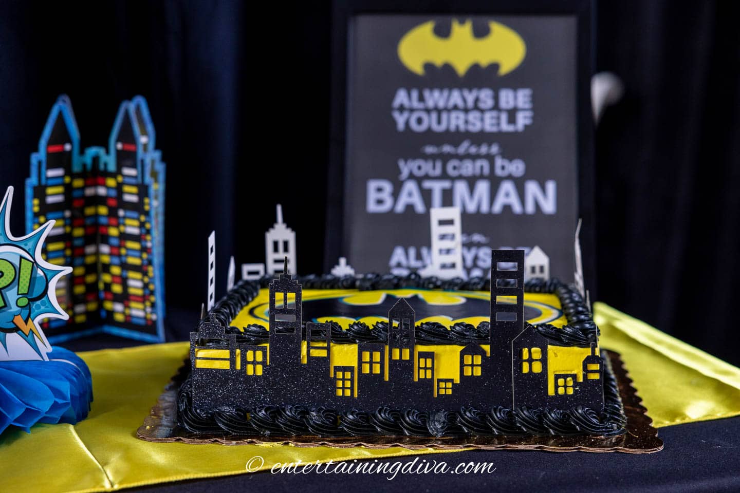 A black and yellow batman cake with a skyline decoration around the outside