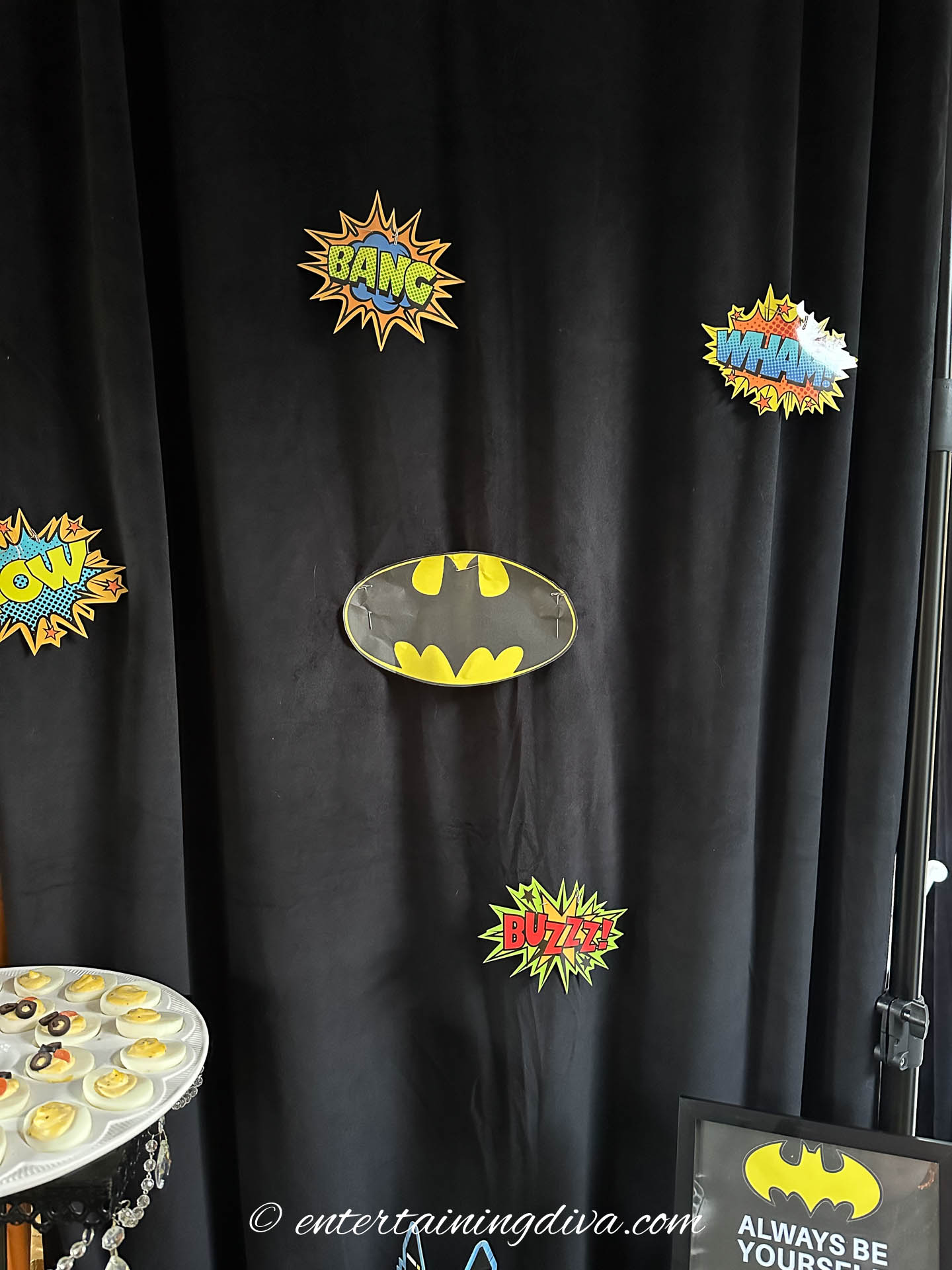 The batman signal and various super hero sayings pinned to a black curtain