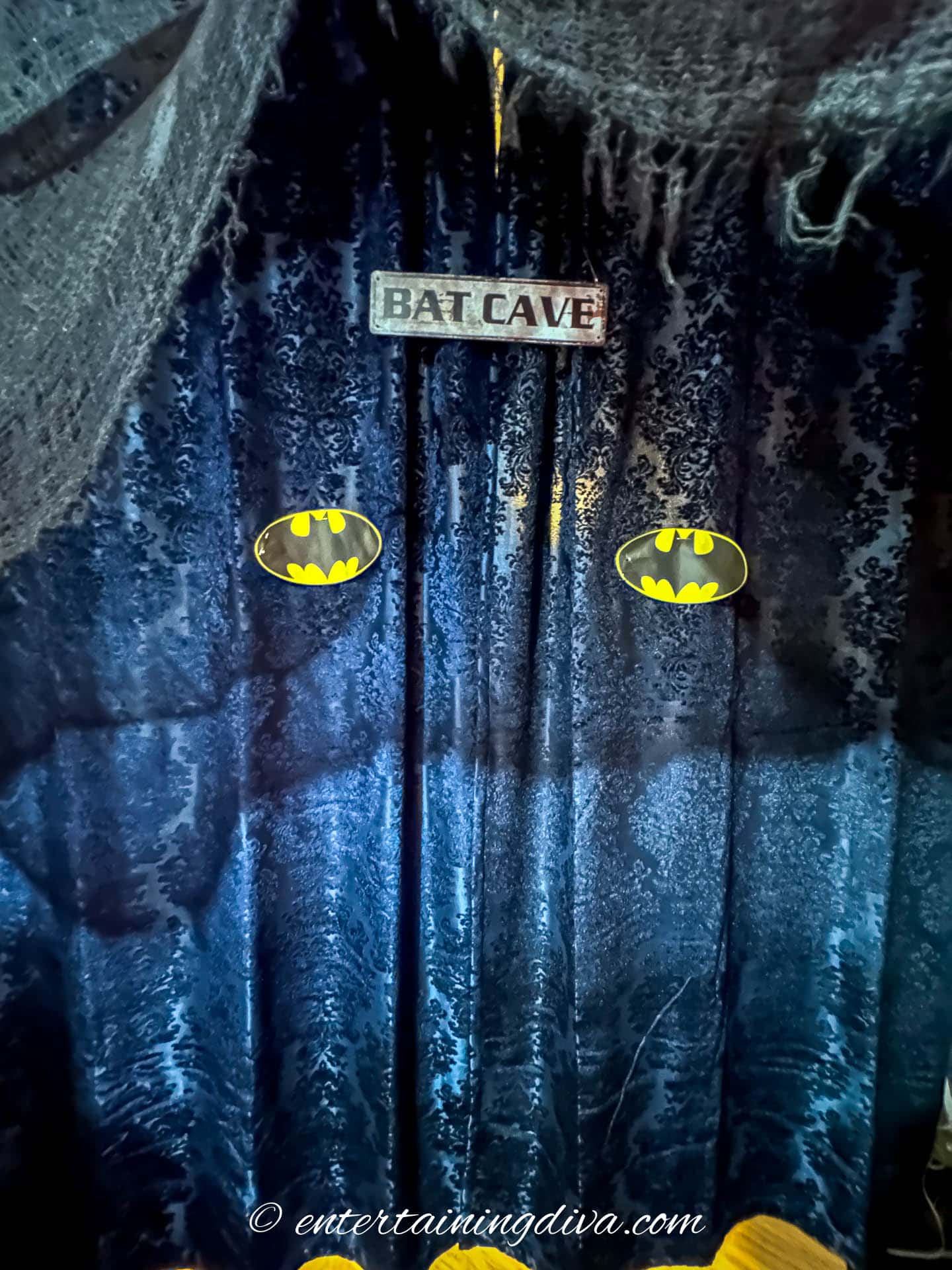 Black curtains with two bat signals and a Bat Cave sign hung on them