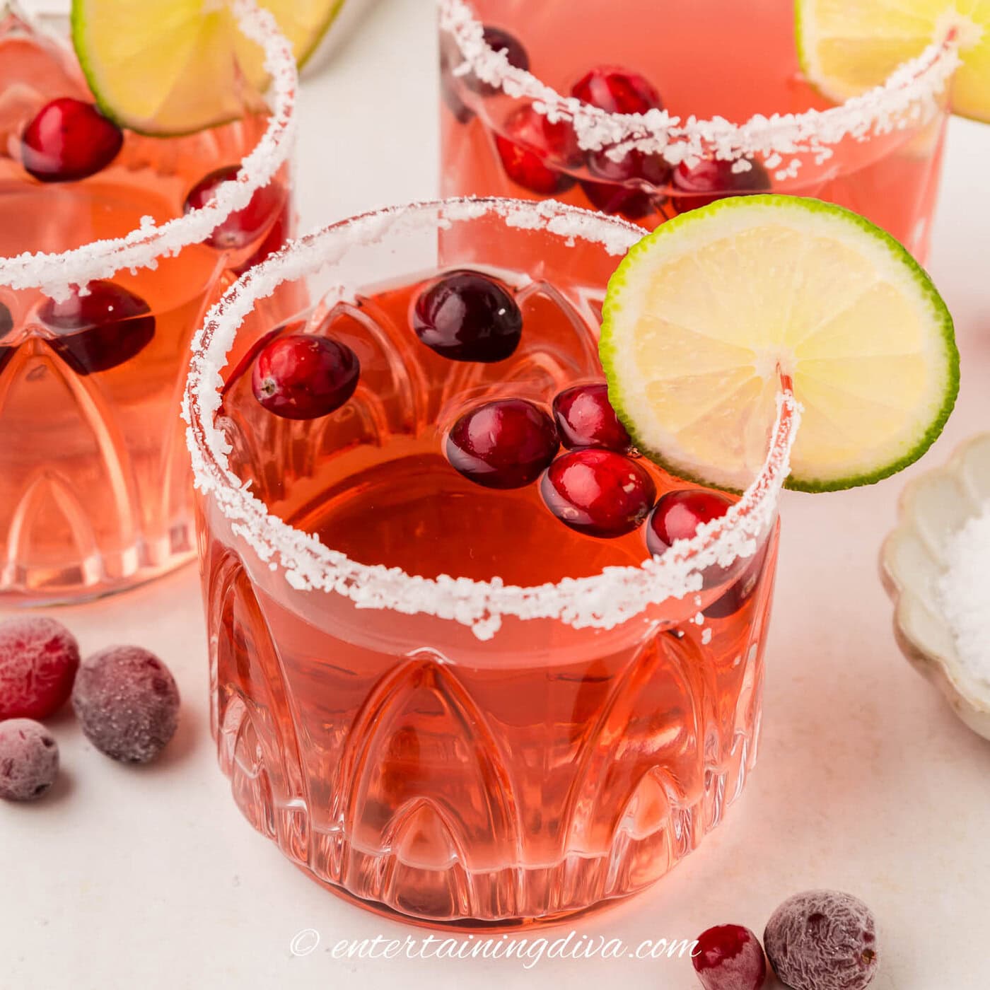 close up of a cranberry margarita garnished with a salt rim, fresh cranberries and a lime wheel