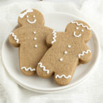 a close up of two gingerbread men on a plate beside some cinnamon sticks and a second plate with gingerbread cookies in the shape of snowflakes