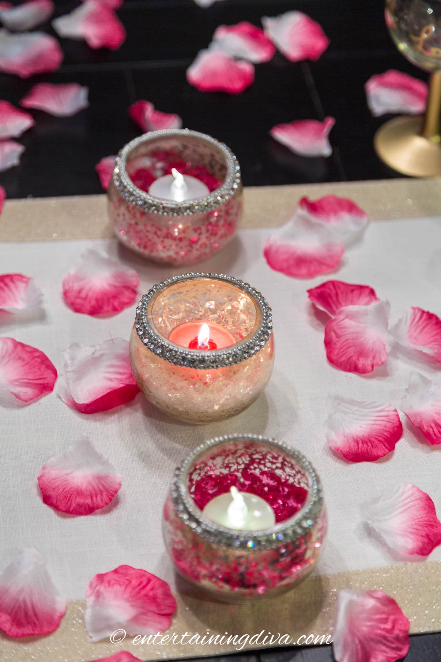 Artificial rose petals on a Valentine's Day table with 3 tealight candles