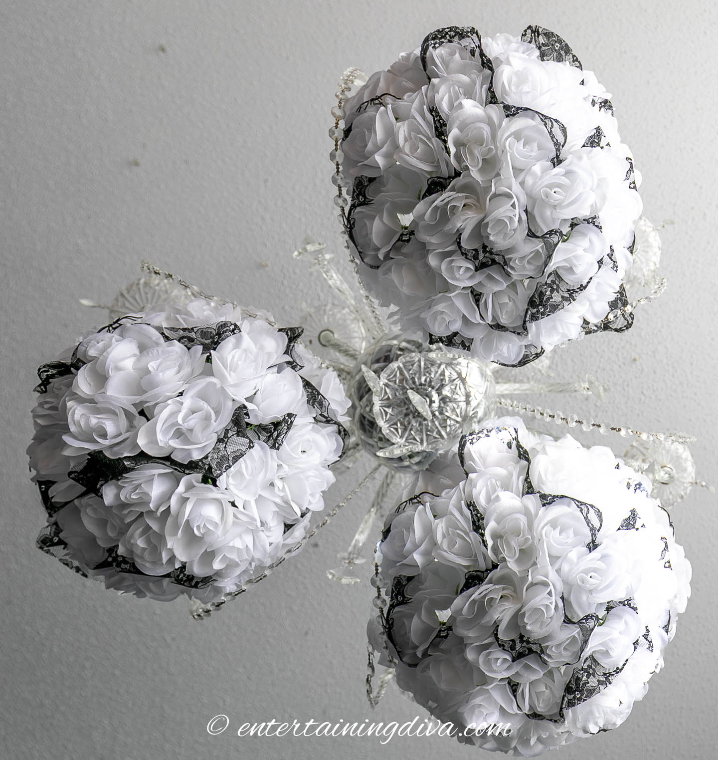 Three spherical white floral arrangements with black lace accents are attached to a central metallic fixture against a light-colored background.