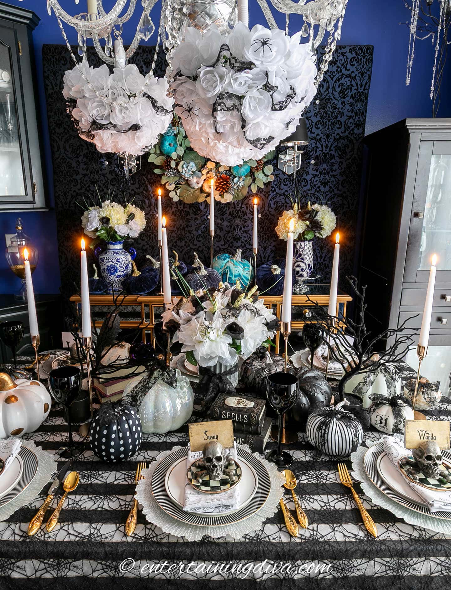 Elegant Halloween-themed dining table with black and white decor, candles, floral centerpieces, and decorative pumpkins arranged for a festive meal.
