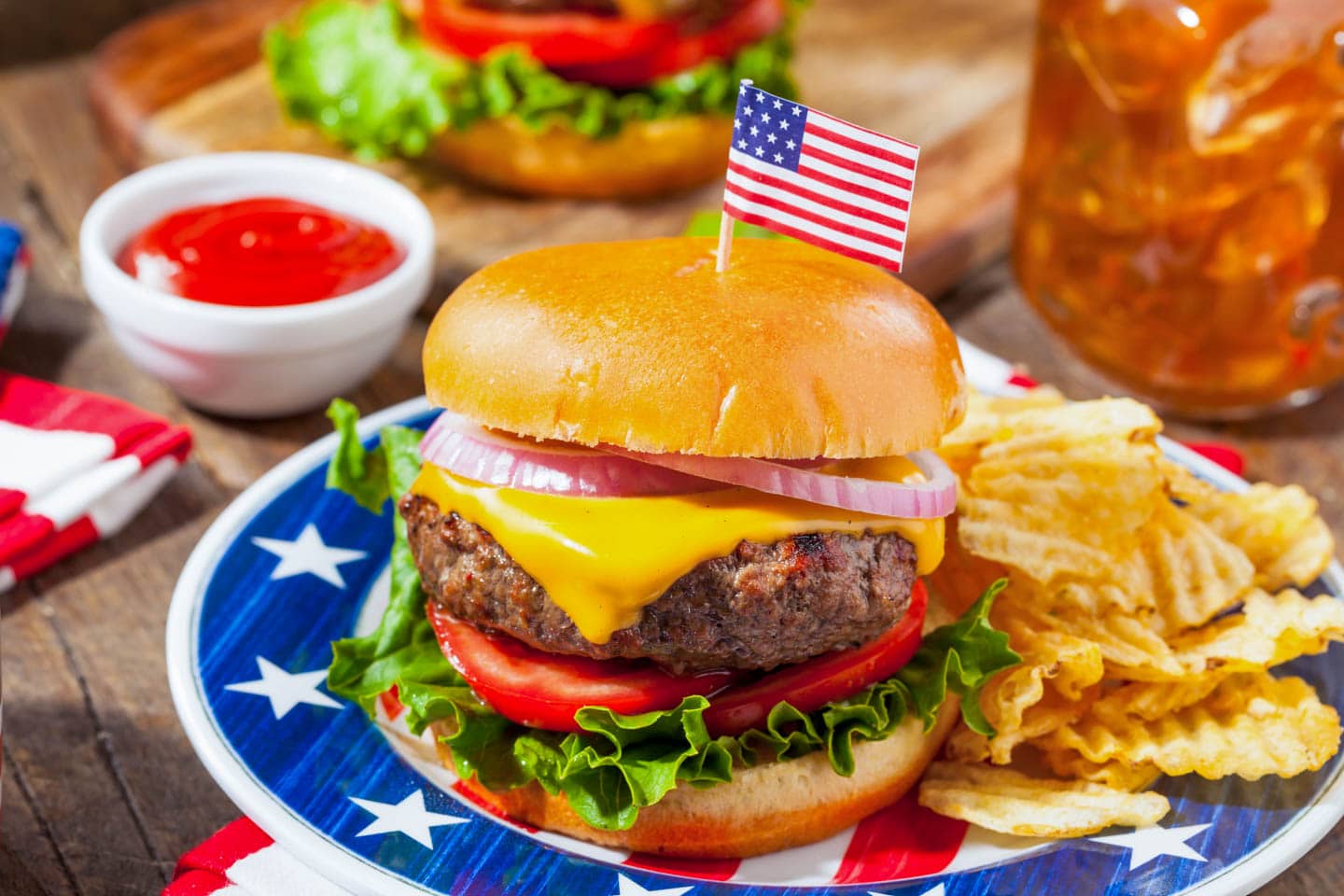 hamburger with an American flag toothpick on top, served with fries on a red, white and blue plate