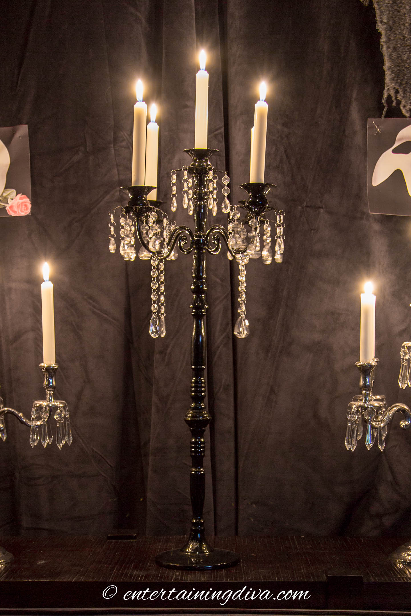 Black candelabra with white candle in front of a black curtain
