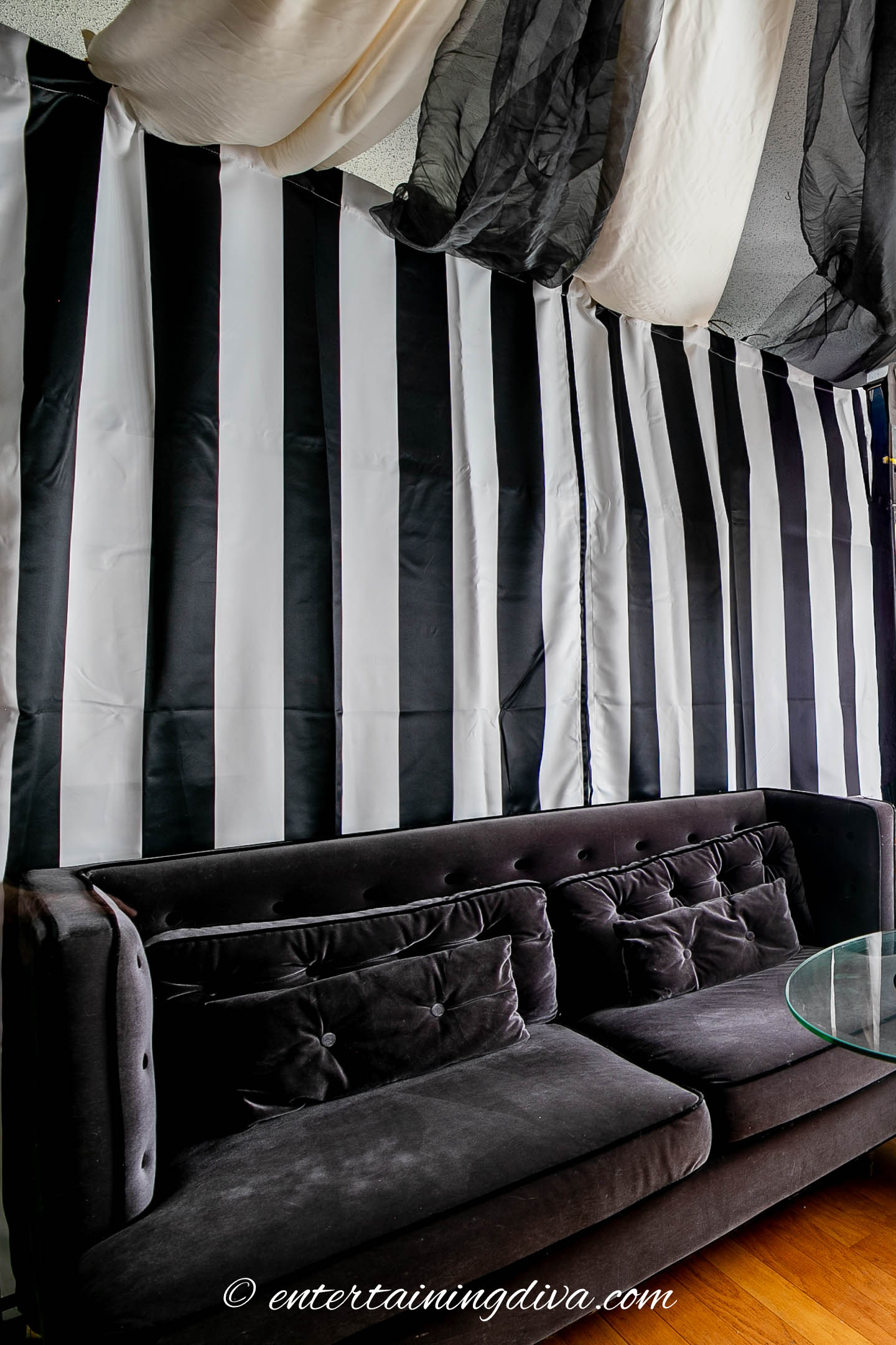 two black sofas with black and white striped curtains hung acround the room and black and white fabric hung from the ceiling