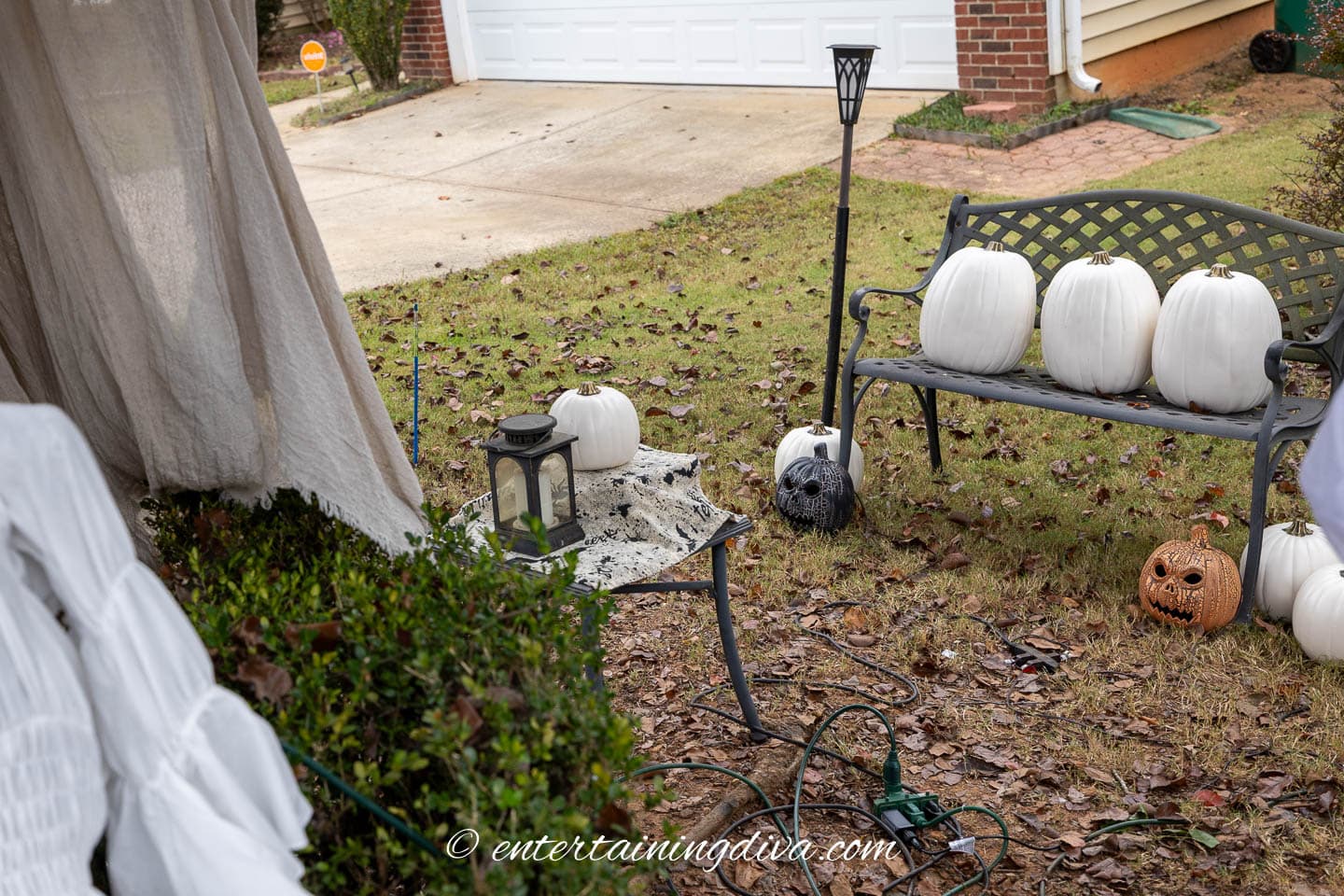 A projector table behind a bush in front of a bench with 3 pumpkins