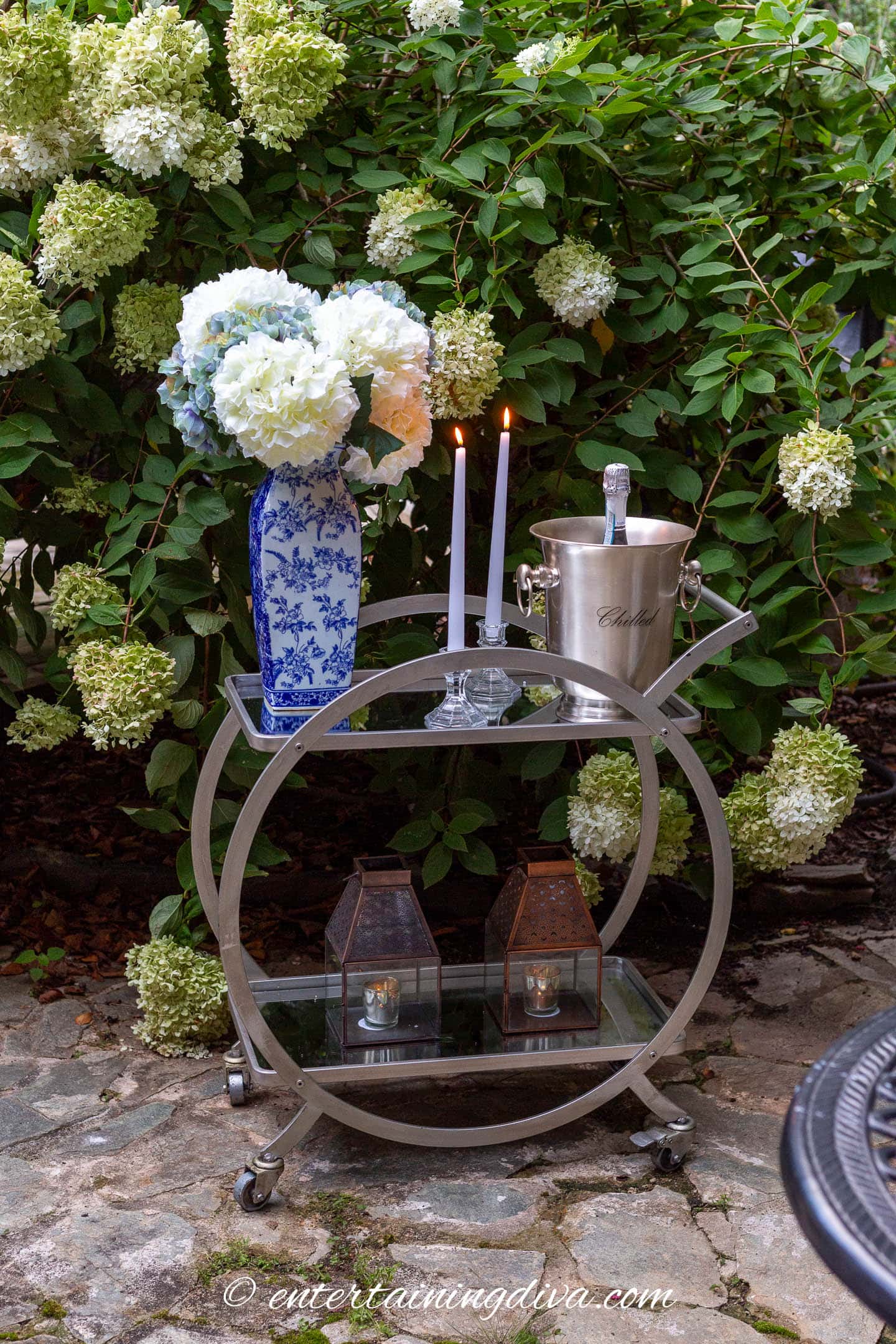 A bar cart with a vase of flowers, candles and a wine chiller on an outdoor patio