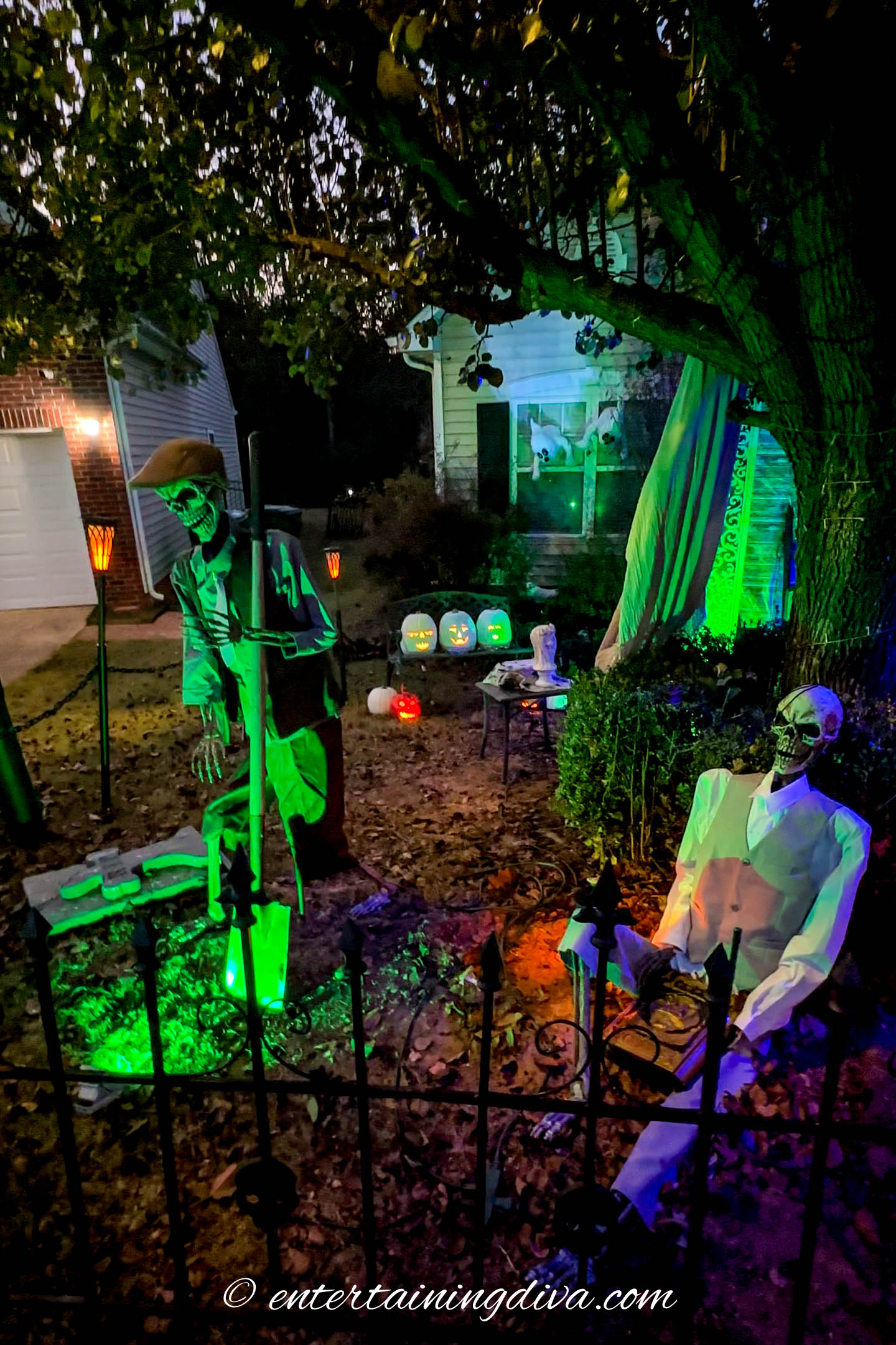 Three singing pumpkins in a Halloween yard with skeletons