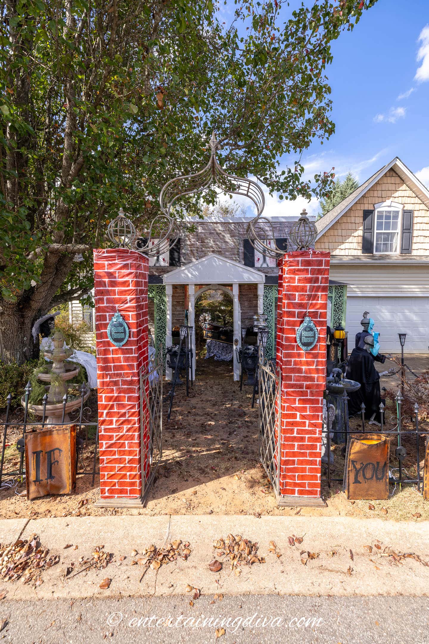 Outdoor Halloween display featuring a brick entrance with iron gates, decorated with skeletons, tombstones, and