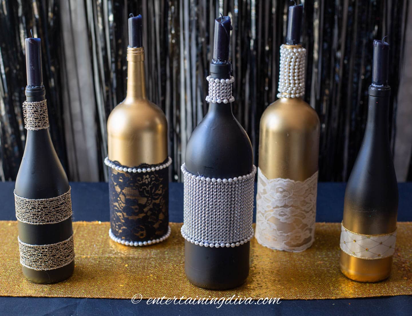 wine bottles spray painted black and gold, and decorated with ribbon and lace for a Phantom of the Opera centerpiece