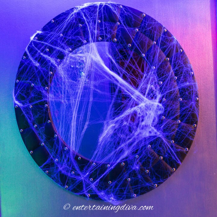 a round mirror covered with glow in the dark stretchy spider webs
