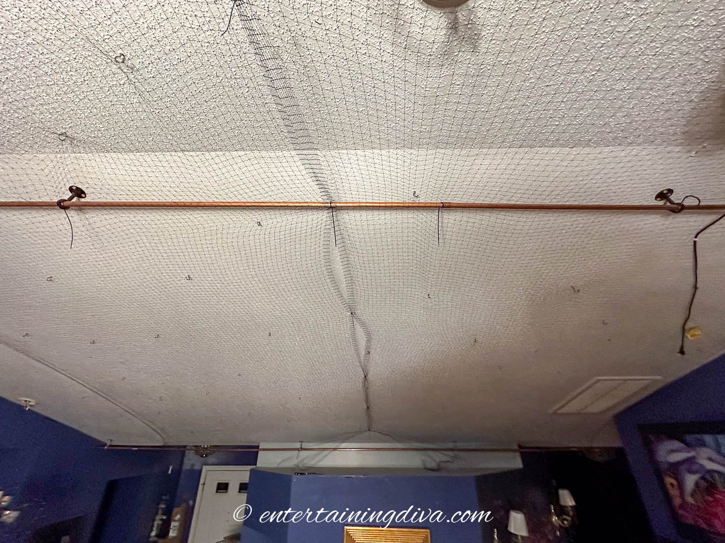 Two curtain rods installed in parallel to each other on a ceiling with black mesh stretched between them