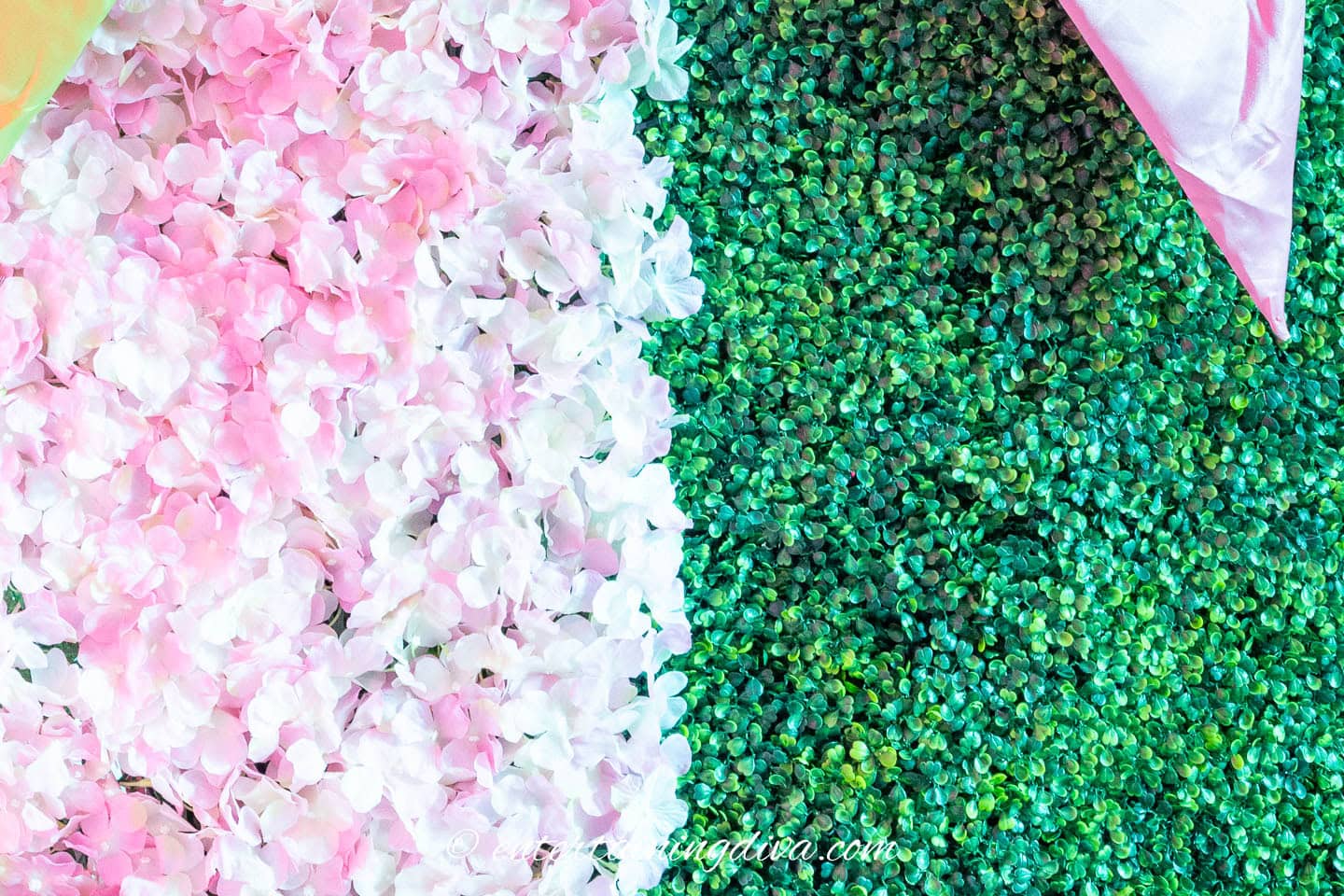 A wall decorated with pink and white artificial flowers on the left and green artificial foliage on the right, divided diagonally.