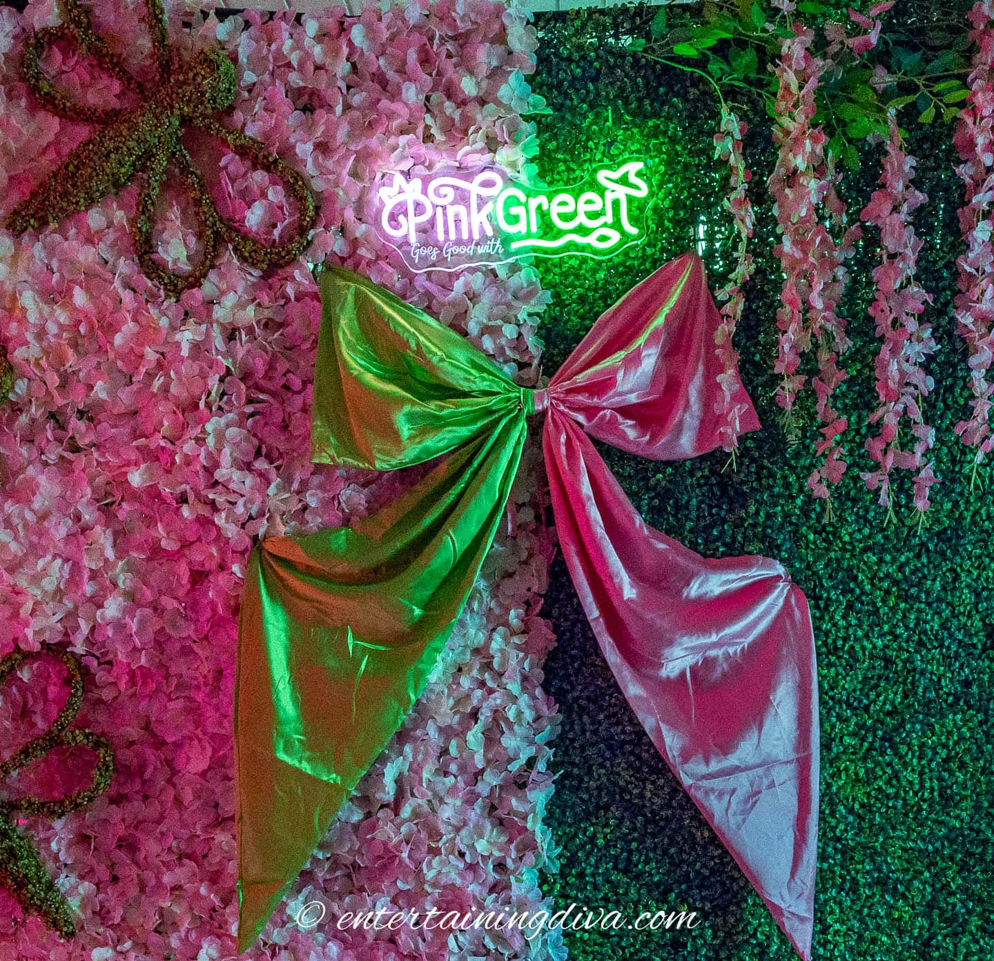 Large metallic pink and green bows decorate a backdrop of pink flowers and green leaves with a neon