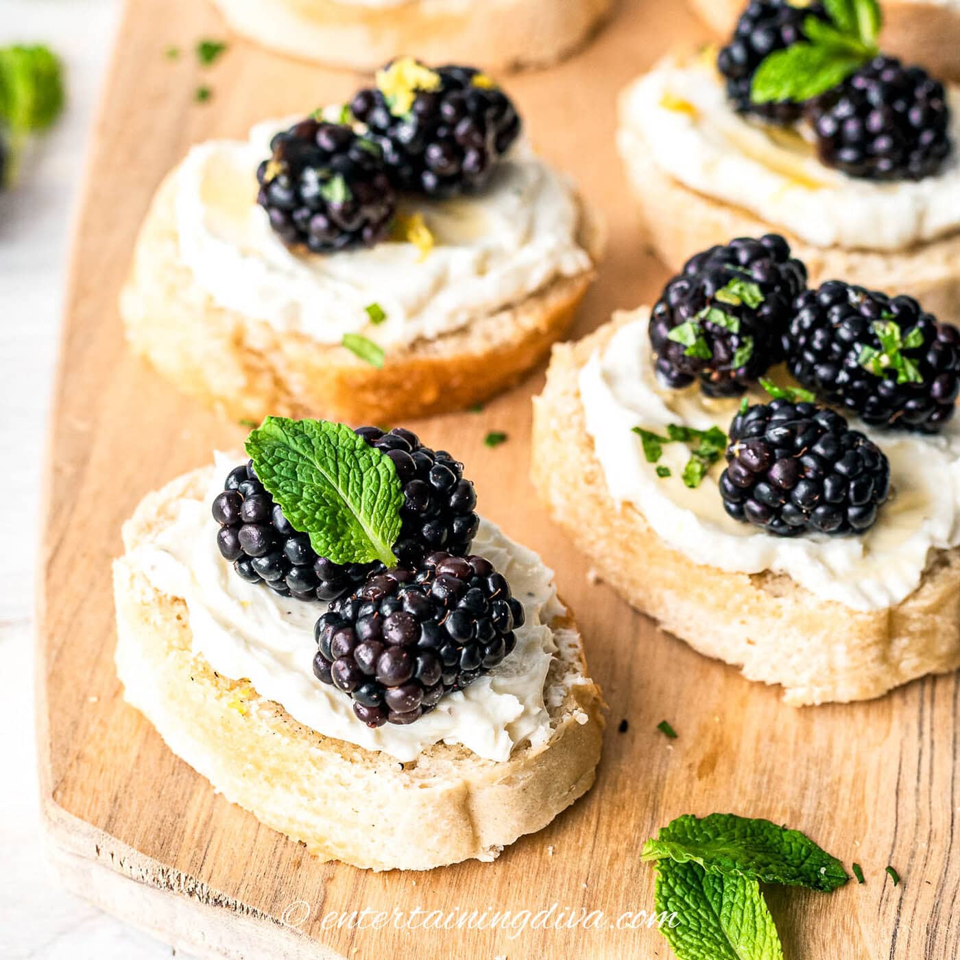 close up of 3 blackberry goat cheese crostini appetizers garnished with mint leaves on a cutting board