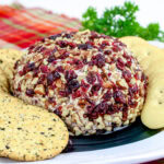 close up of cranberry pecan cheese ball on a plate with crackers