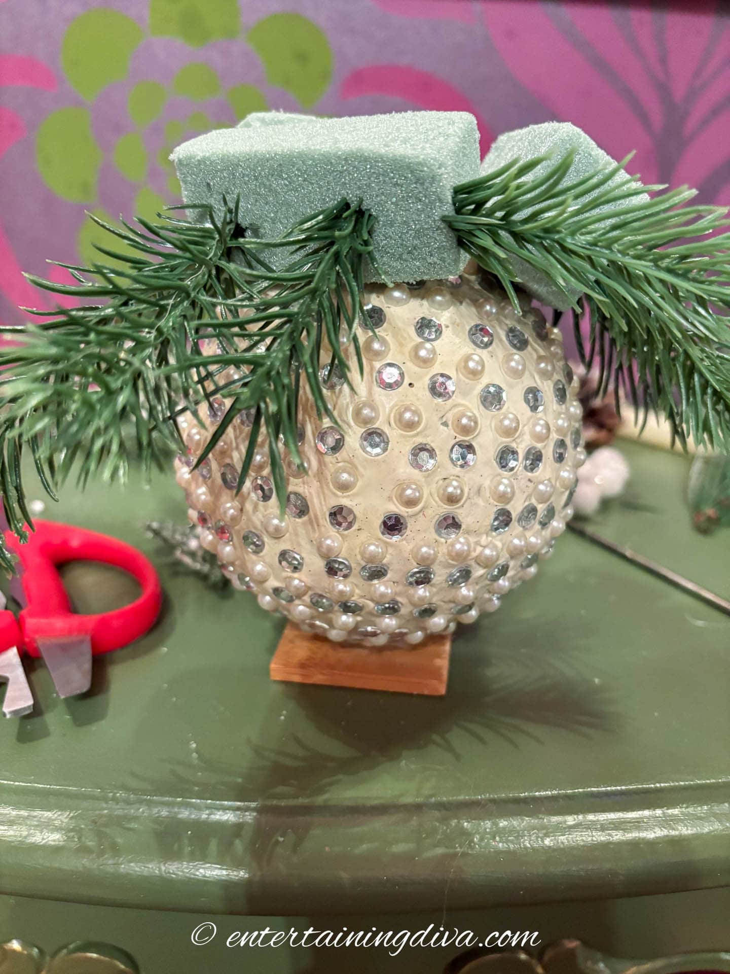 Artificial evergreen picks being attached to a Christmas ornament centerpiece