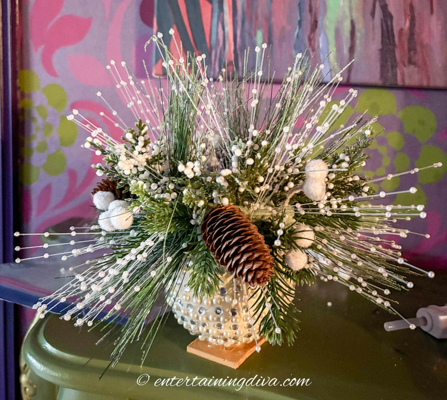A small DIY Christmas ornament centerpiece decorated with artificial evergreen and white pearl picks