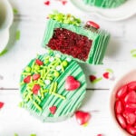 Close up of a Grinch cake puck with a bite taken out of it showing the red velvet cake inside