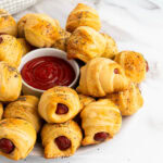 close up of pigs in a blanket on a plate with a bowl of ketchup in the middle