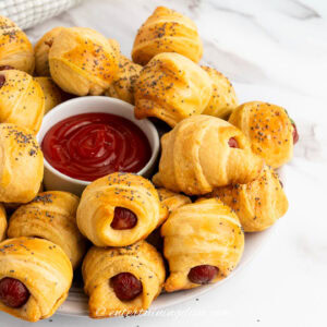 close up of pigs in a blanket on a plate with a bowl of ketchup in the middle