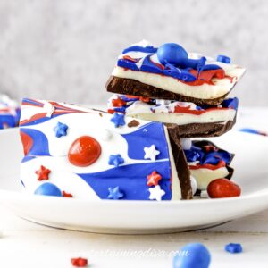 A plate of layered chocolate bark decorated with red, white, and blue swirls, star-shaped sprinkles, and candy pieces.