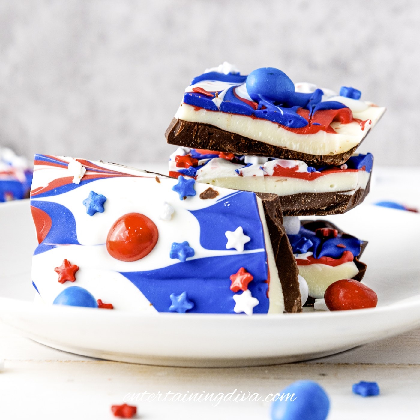 A plate of layered chocolate bark decorated with red, white, and blue swirls, star-shaped sprinkles, and candy pieces.