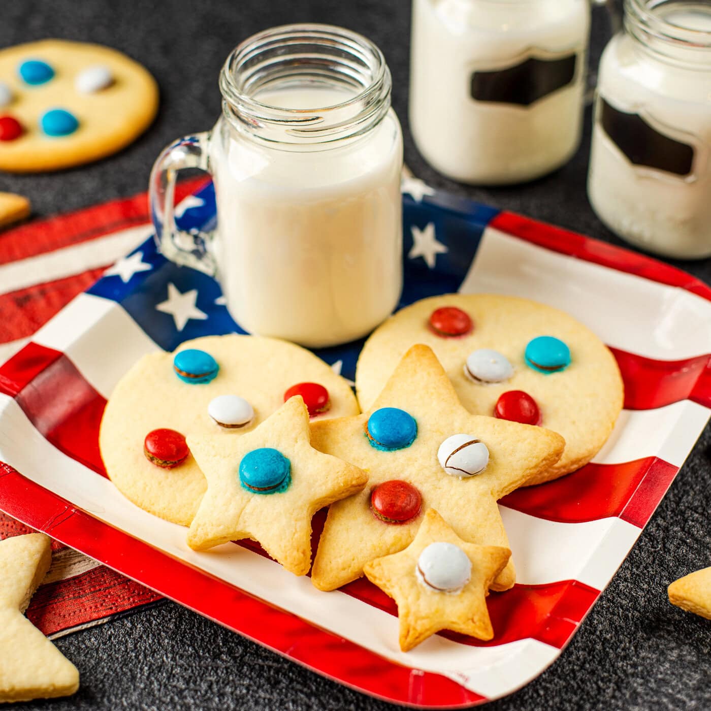 shortbread cookies with red, white and blue M&M's on an American flag plate with a glass of milk