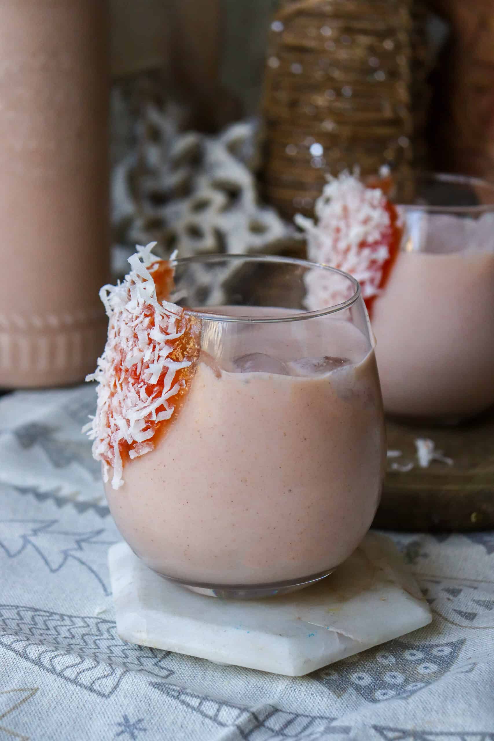 Two glasses of pink smoothie with coconut flakes on top.