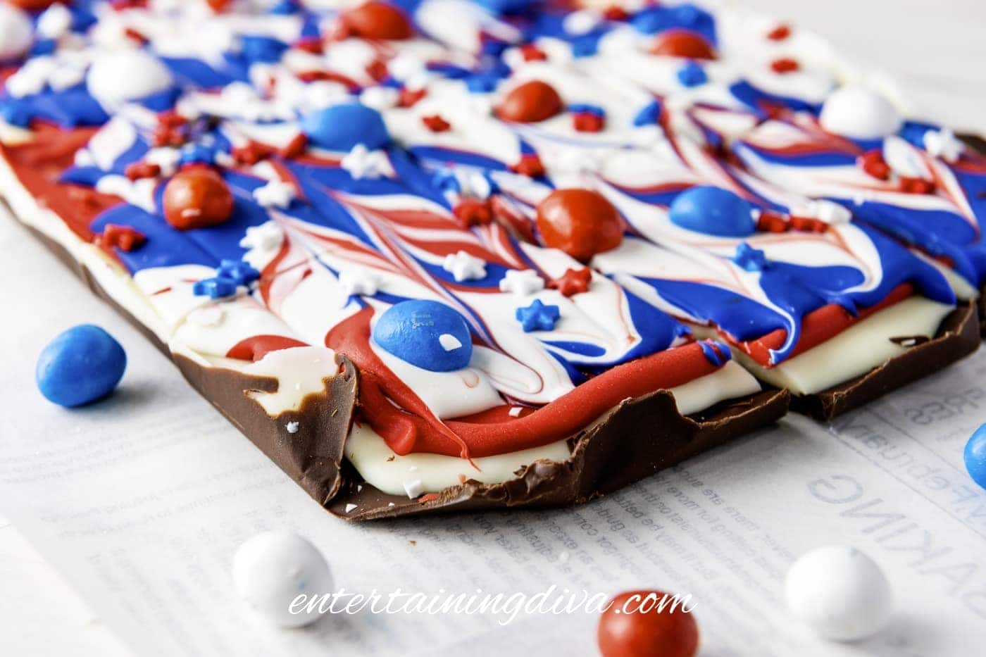 A chocolate bark topped with swirled red, white, and blue candy melts and decorated with star-shaped sprinkles and colored candies.
