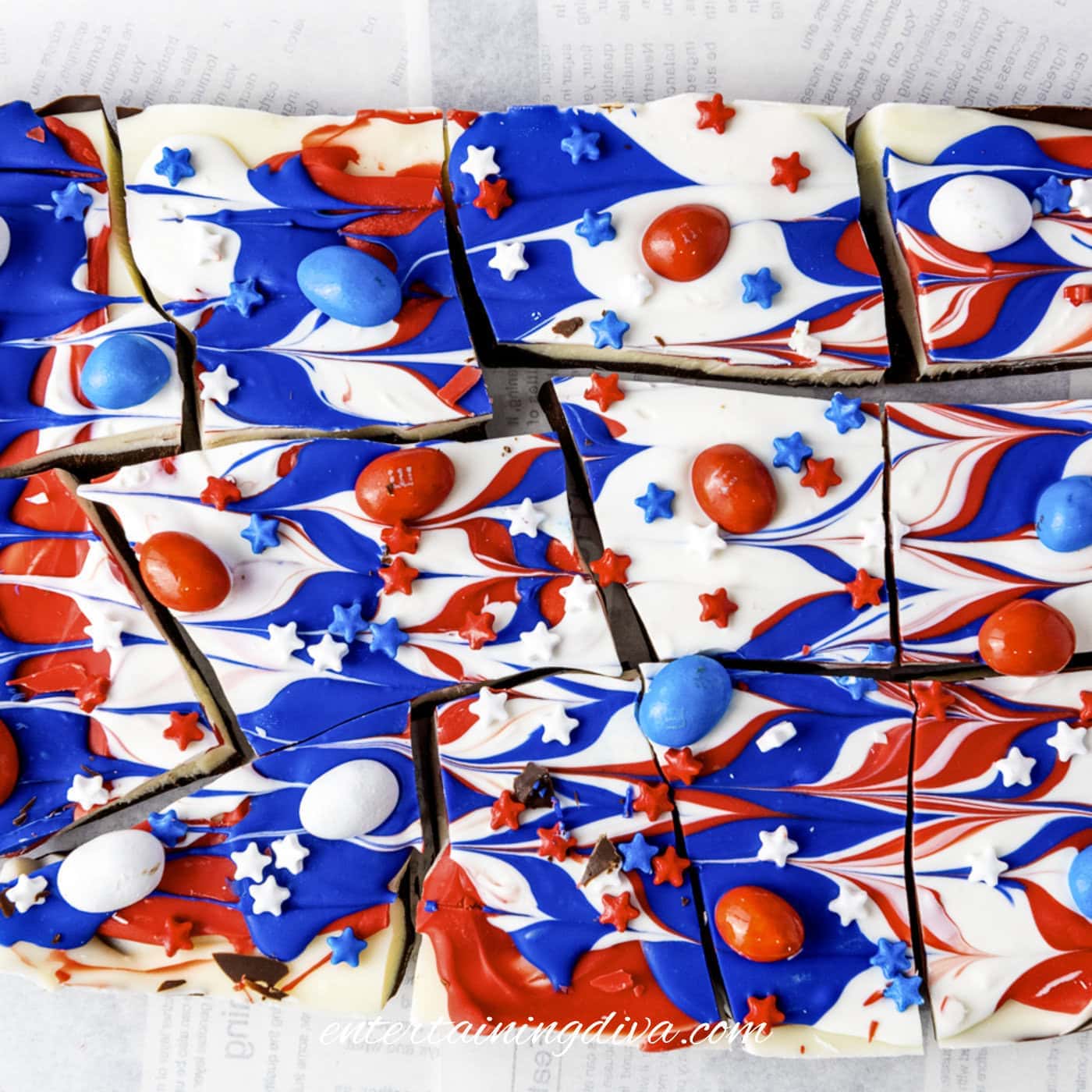 Pieces of chocolate bark with swirled red, white, and blue icing, star-shaped sprinkles, and red, white, and blue candies on parchment paper.