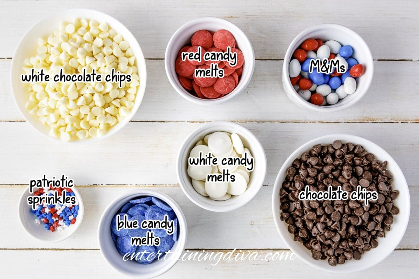 Various baking ingredients in bowls on a white surface, including white chocolate chips, red and blue candy melts, M&Ms, chocolate chips, white candy melts, and patriotic sprinkles.