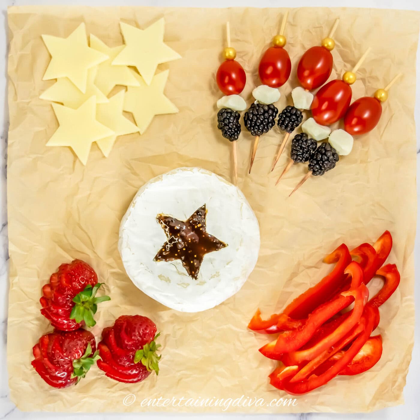 Cheese cut into stars, skewers made with cherry tomatoes, mozzarella pearls and blackberries, a round of brie with a star cut out of the middle, sliced strawberries and sliced red peppers