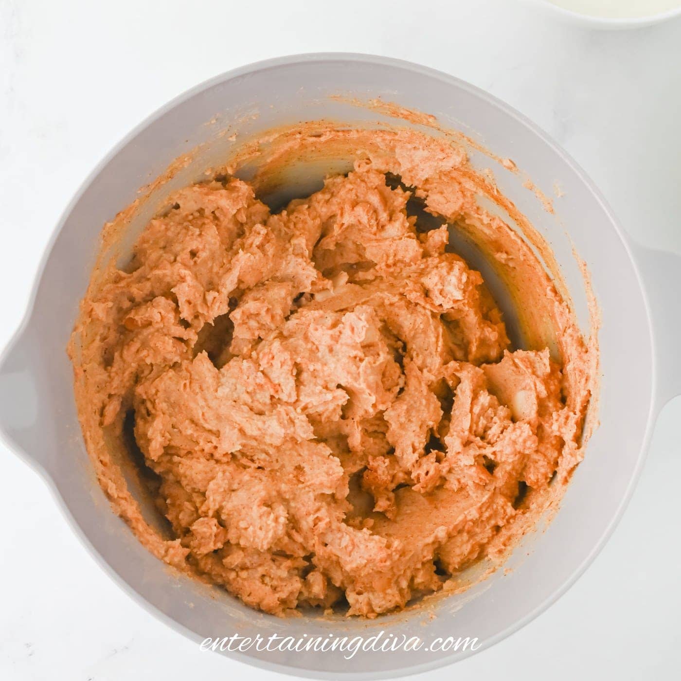 A mixing bowl filled with refried beans sits on a white surface, with two small bowls nearby.