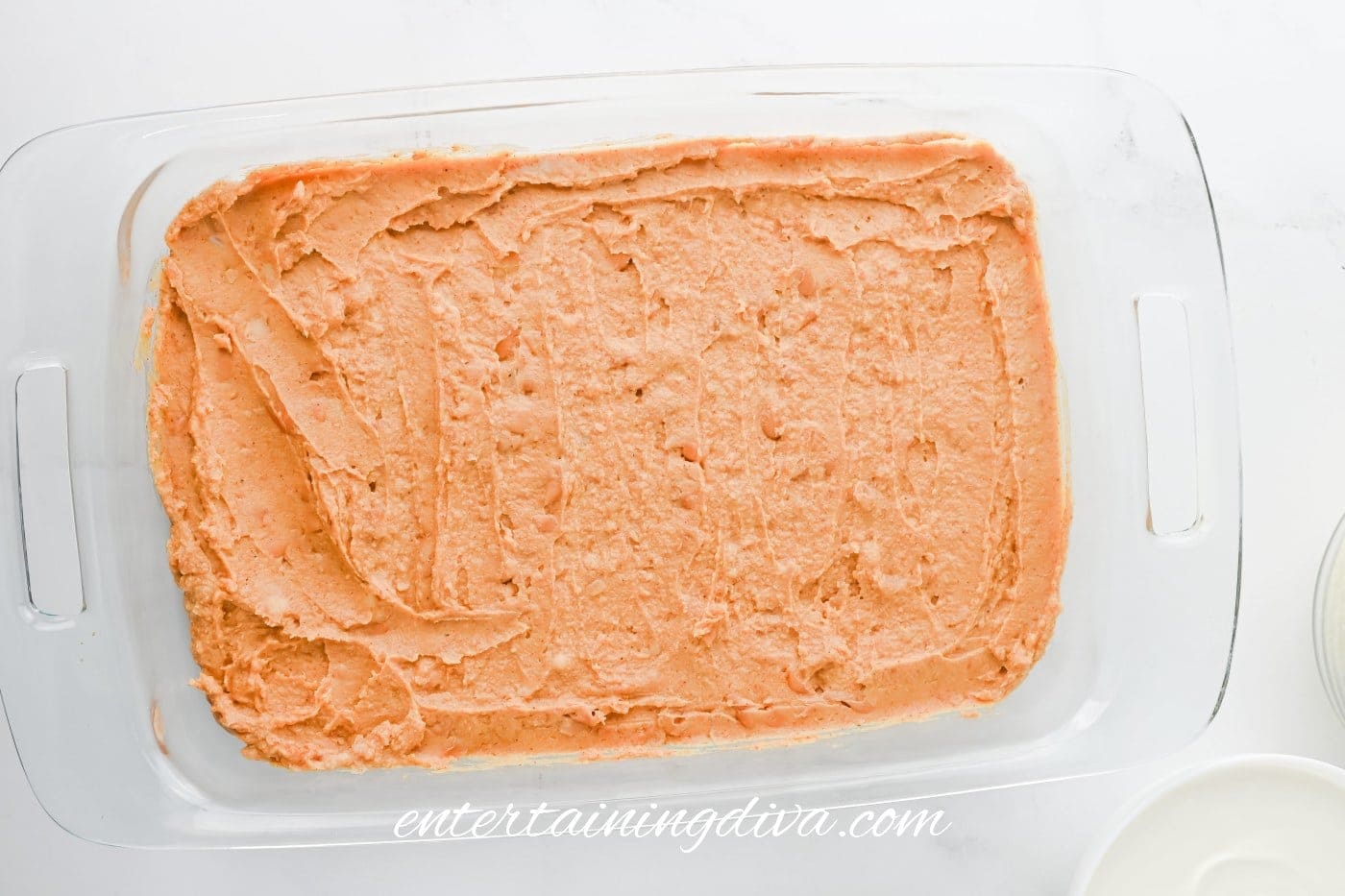Rectangular glass baking dish filled with a smooth, evenly spread layer of refried beans