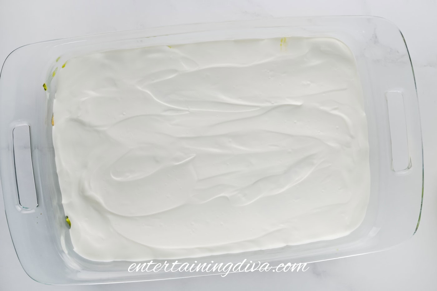 A glass baking dish filled with a layer of smooth, sour cream spread evenly over the surface of the guacamole.