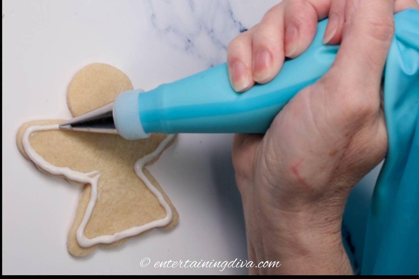 Christmas angel sugar cookie being outlined with white royal icing