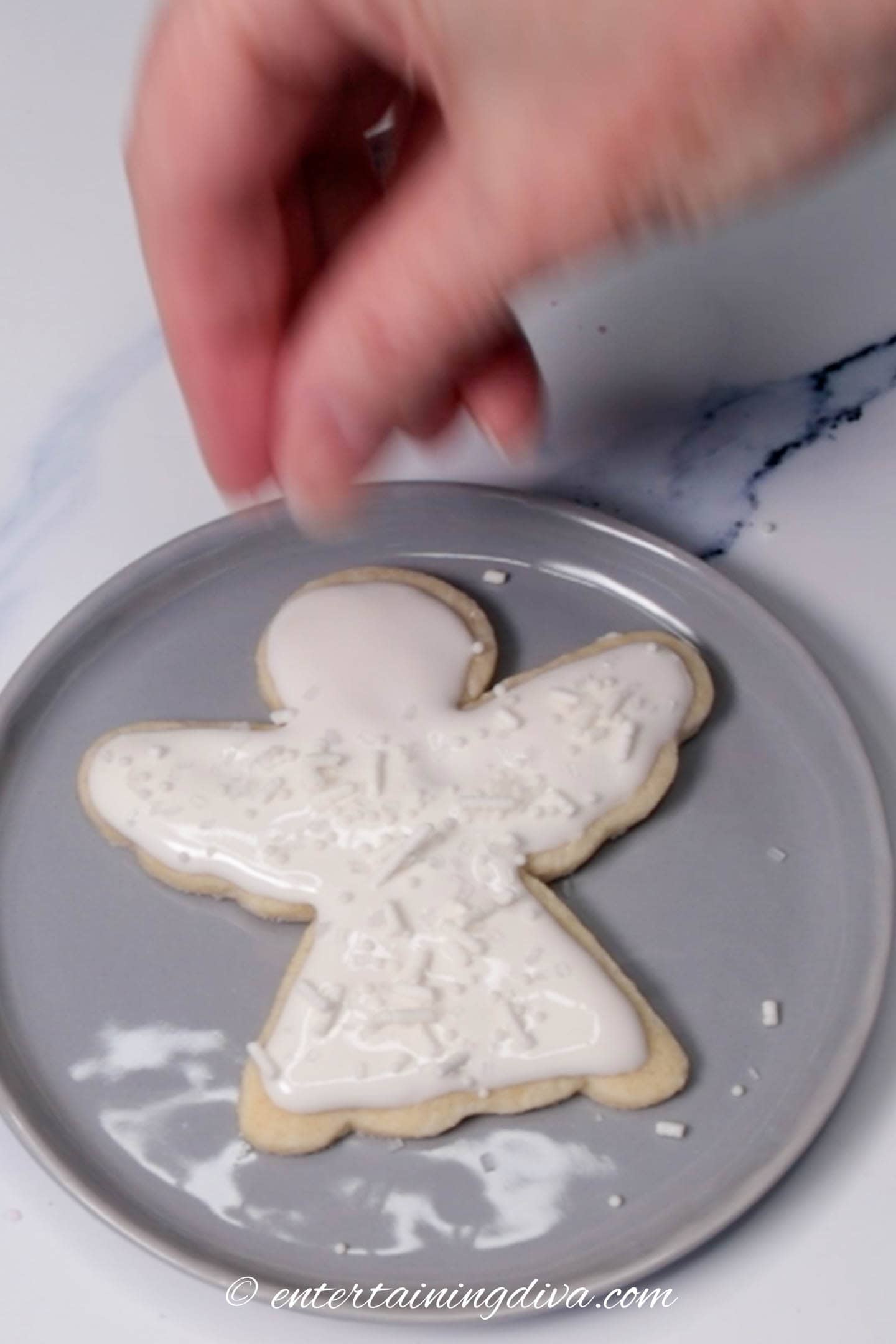 Sprinkles being dropped onto the iced cookie