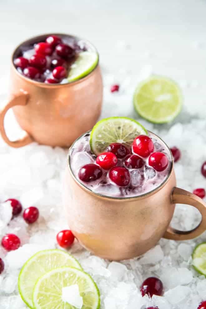 Two copper mugs with cranberries and limes.