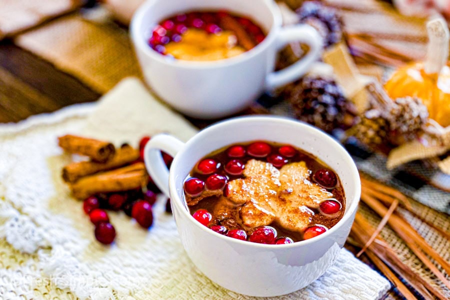 Two mugs of coffee with cranberries on a table.