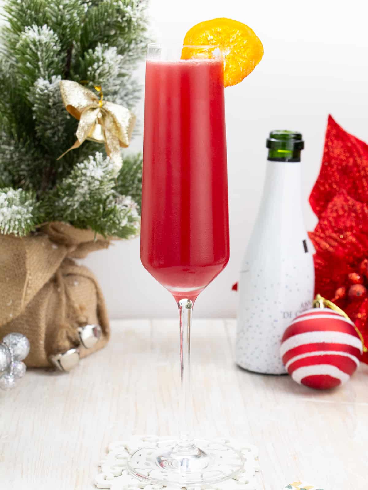 A glass of red wine with a slice of orange sitting on a table next to a christmas tree.