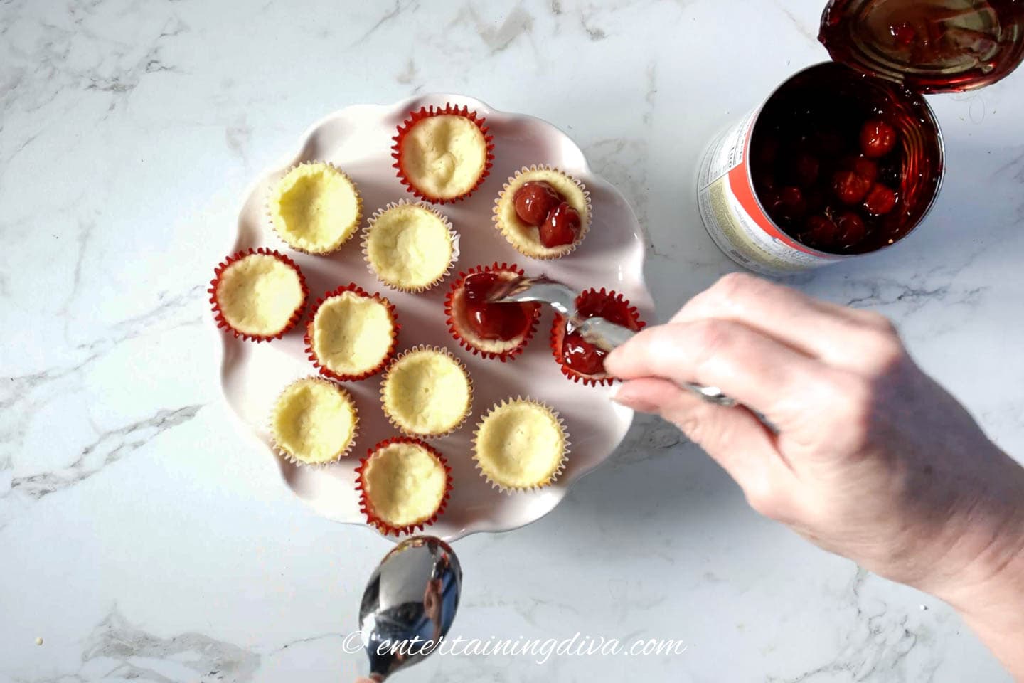Cherry pie filling being spooned onto mini cheesecakes