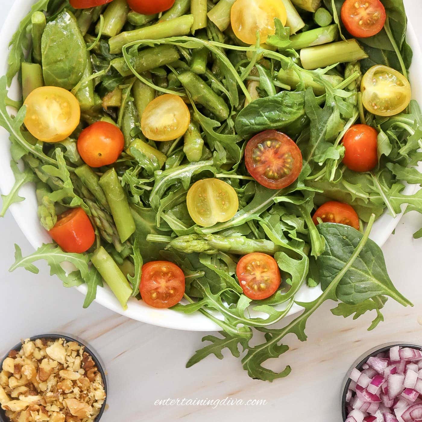 A salad bowl with asparagus, mixed greens and halved cherry tomatoes in it.