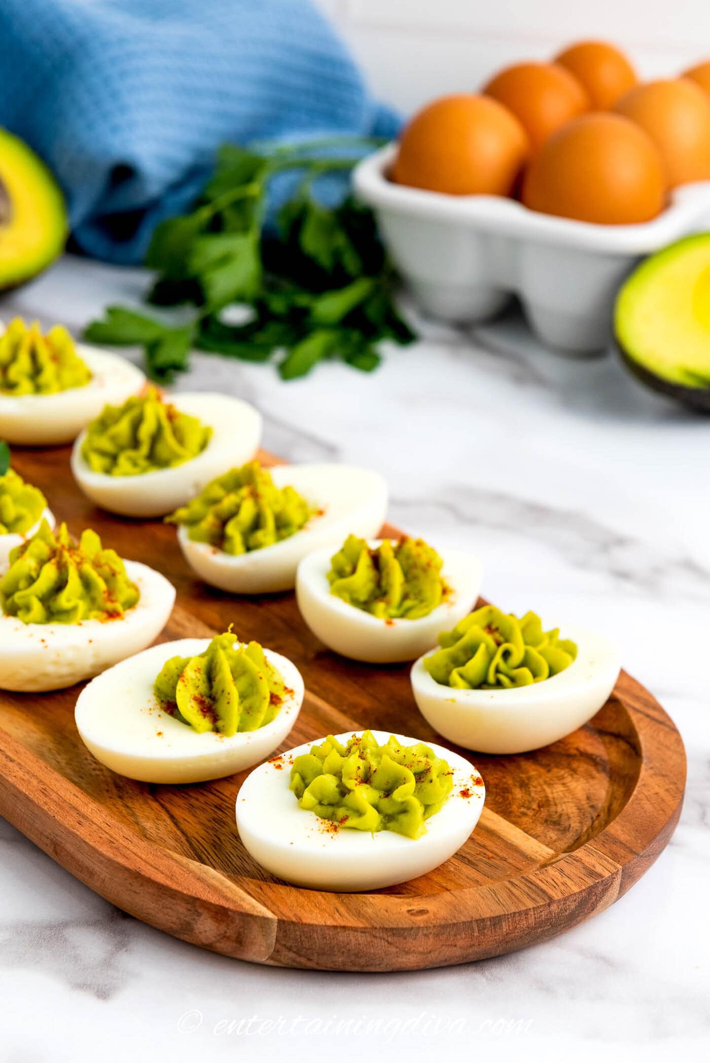 avocado deviled eggs on a wood tray with eggs and parsley in the background